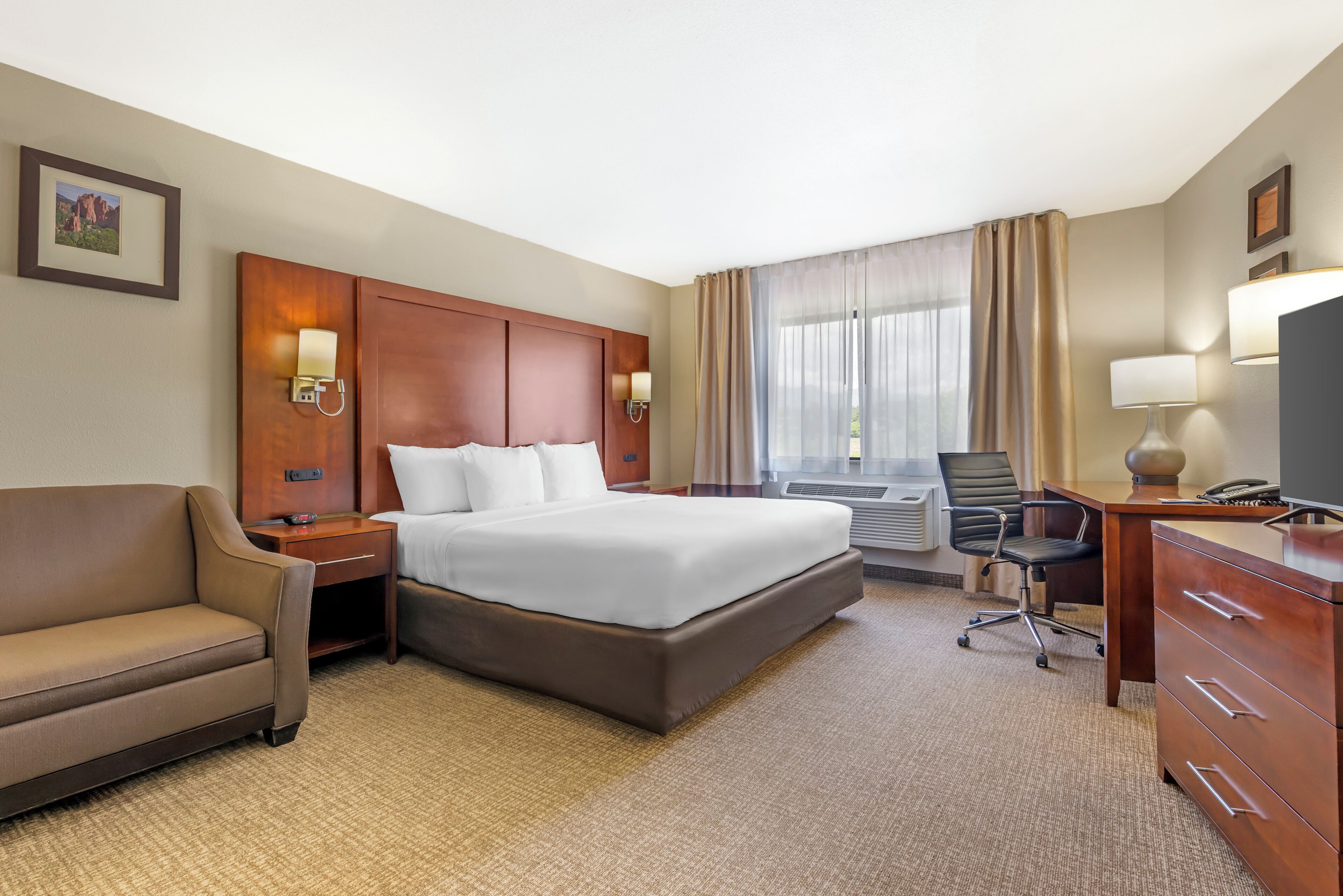 Une chambre d’hôtel avec un grand lit, un bureau, une chaise, un canapé et un téléviseur.