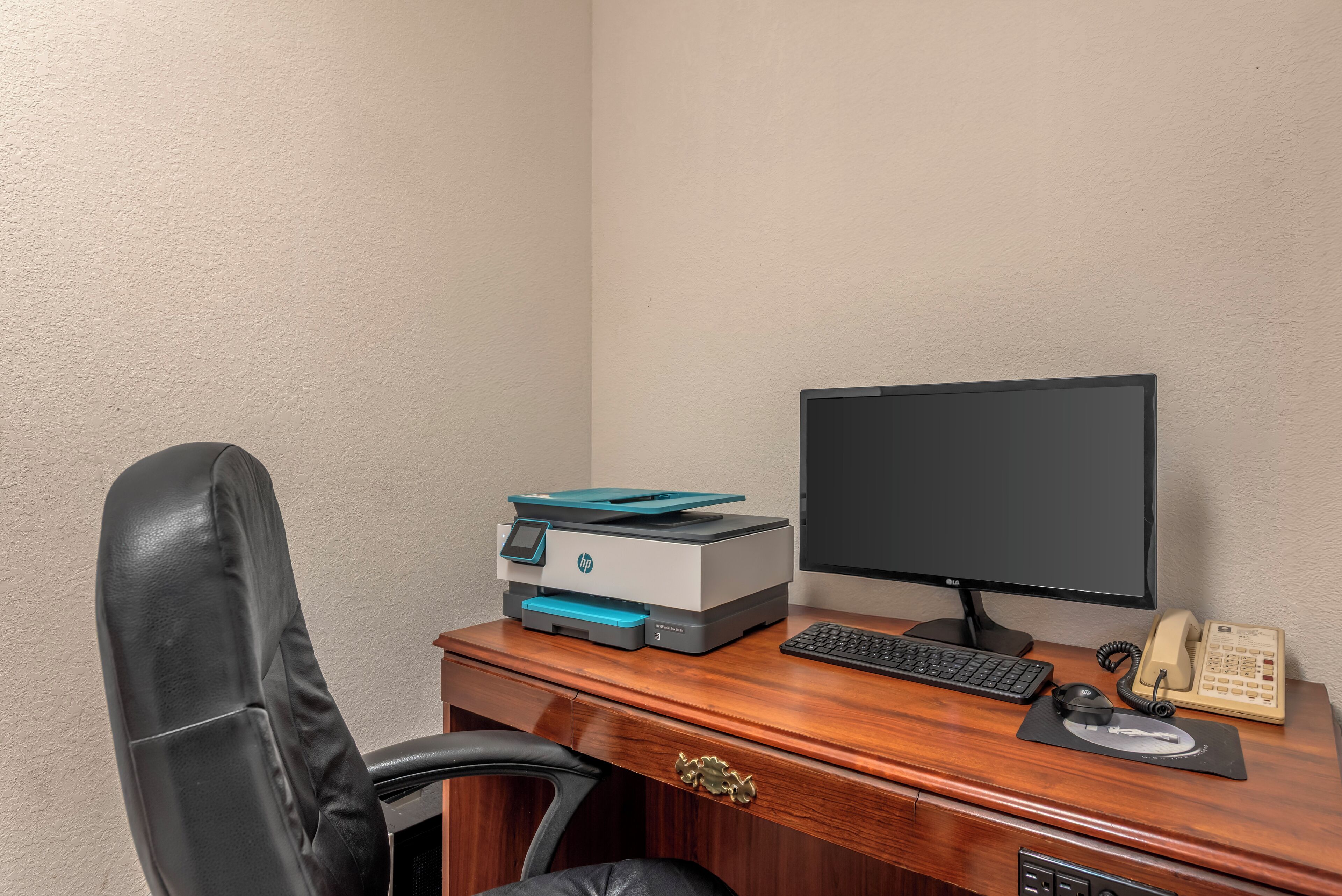 A wooden desk with a printer, a computer monitor, a keyboard, a mouse, and a telephone.