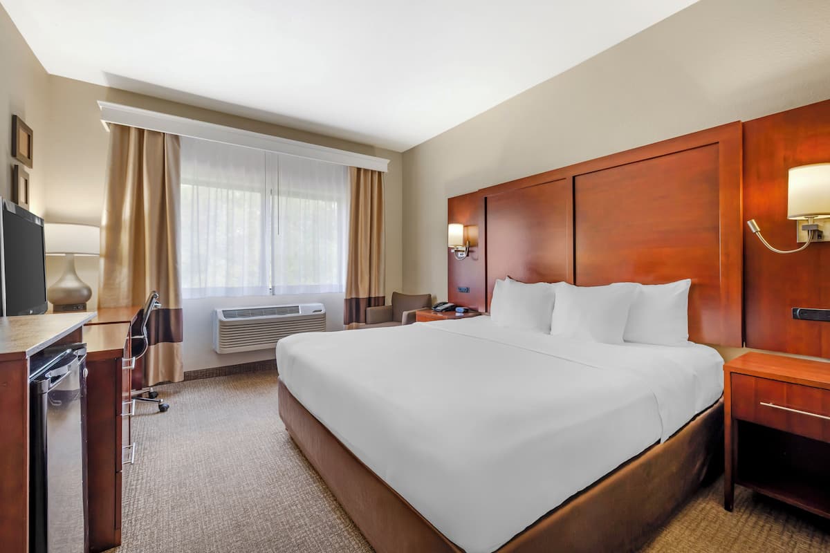 Ein Hotelzimmer mit einem großen Bett, einem Schreibtisch mit Stuhl, einer Schreibtischlampe, einem Nachttisch und einer Wandleuchte.