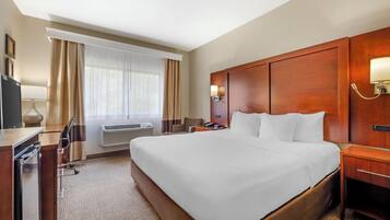 Habitación de hotel con una cama grande, un escritorio con silla, una lámpara de escritorio, una mesita de noche y una lámpara de pared.