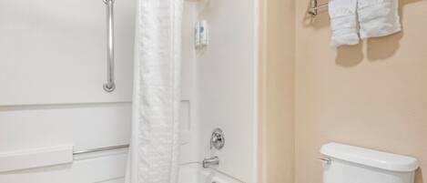 Et badeværelse med badekar, brusebad, toilet og et håndklædetørrestativ med håndklæder.