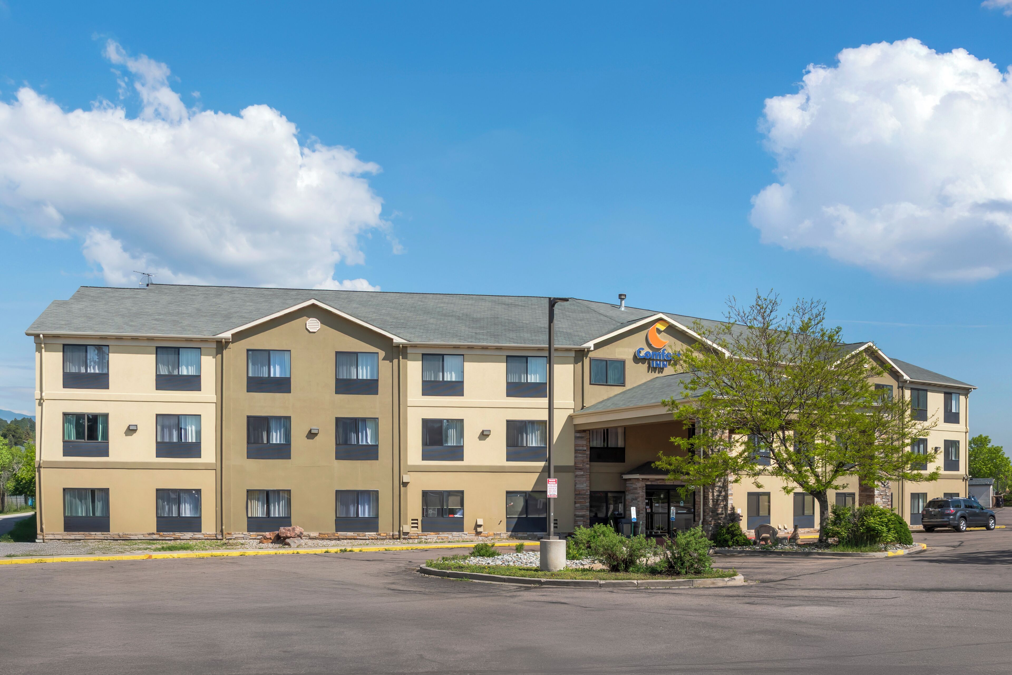 A multi-story hotel with a flat roof, a central entrance, and a parking lot.
