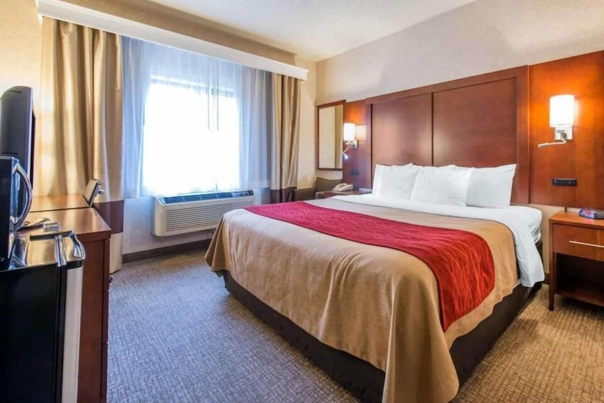Ein Hotelzimmer mit Bett, Schreibtisch, Stuhl, Fernseher, Lampe und einem Fenster mit Vorhängen.