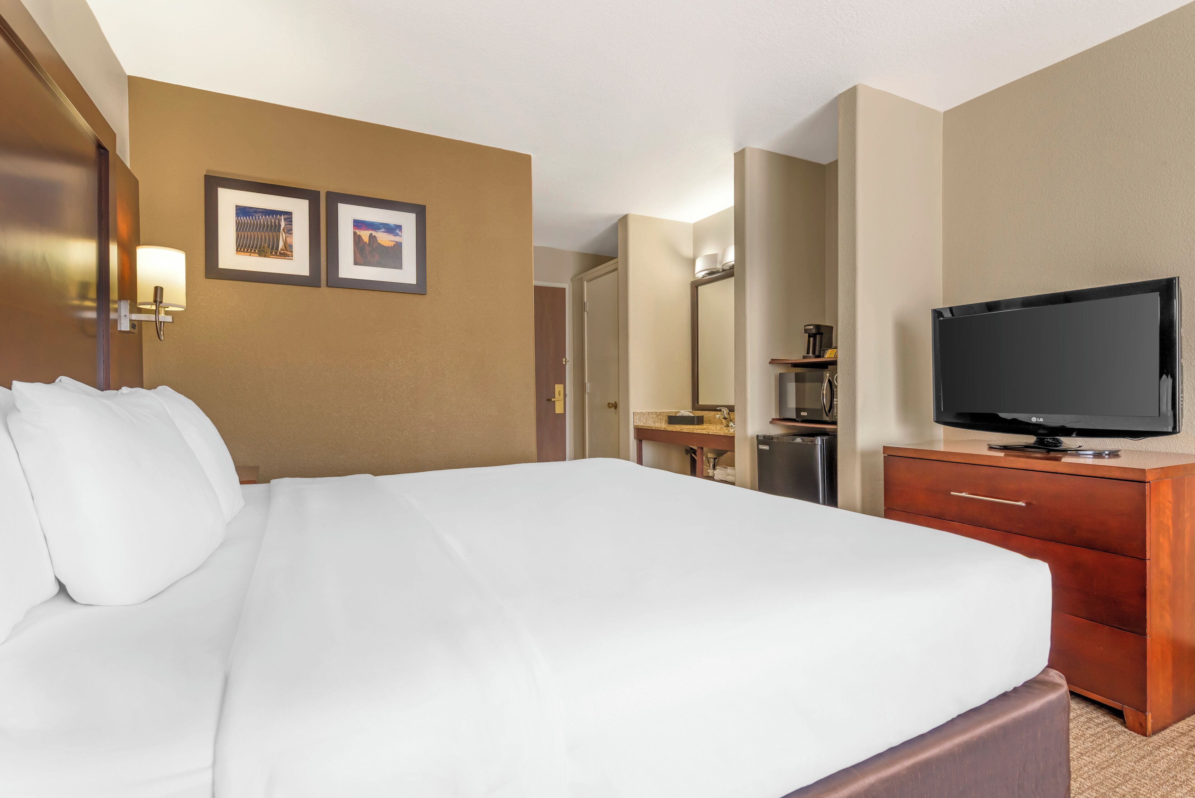 A hotel room with a large bed, a TV, a dresser, and a desk with a lamp.