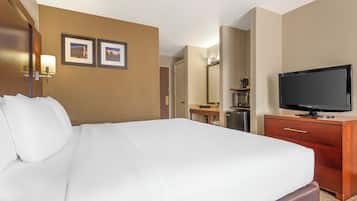 A hotel room with a large bed, a TV, a dresser, and a desk with a lamp.