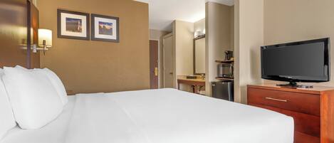 A hotel room with a large bed, a TV, a dresser, and a desk with a lamp.