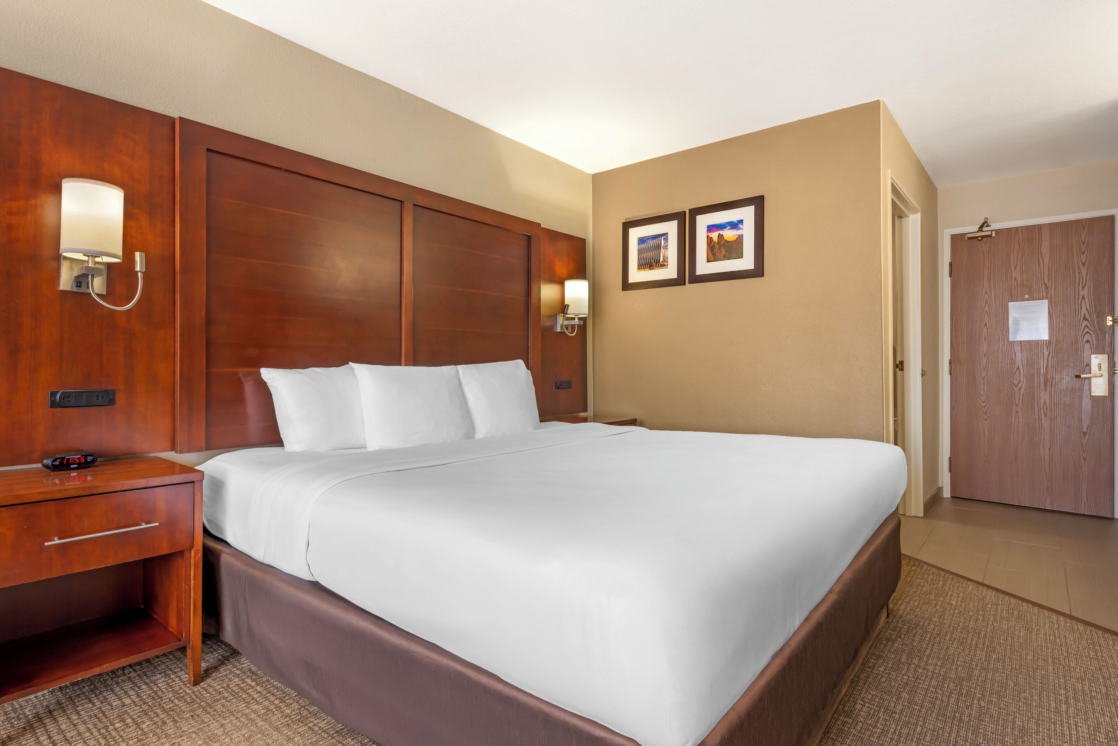 A hotel room with a large bed, wooden headboard, bedside tables, and wall-mounted lamps.