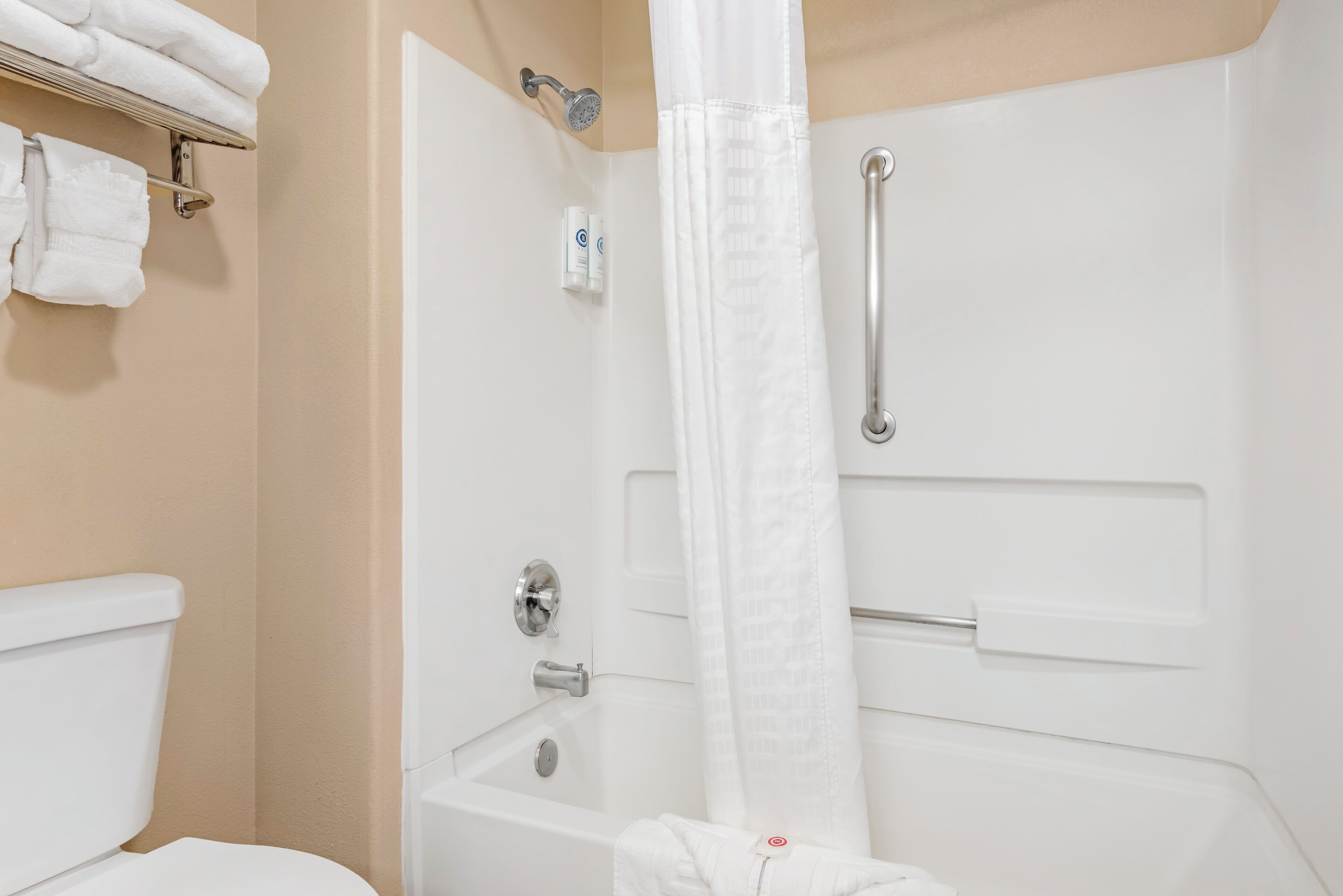 A bathroom with a toilet, a shower with a grab bar, and a towel rack with folded towels.