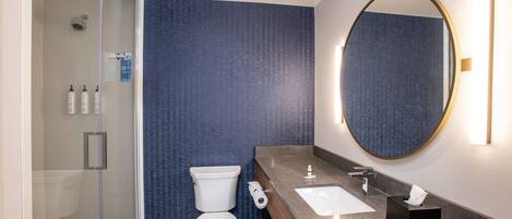 A modern bathroom with a glass shower enclosure, a toilet, a sink with a mirror, and toiletries on the wall.