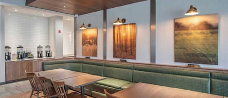A restaurant with a green cushioned bench seating area, wooden tables, and wall-mounted pendant lights.