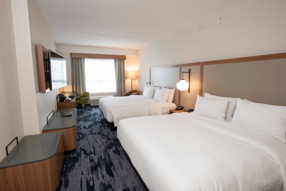 Una habitación de hotel con dos camas, un escritorio, una silla, un televisor y una ventana con cortinas.