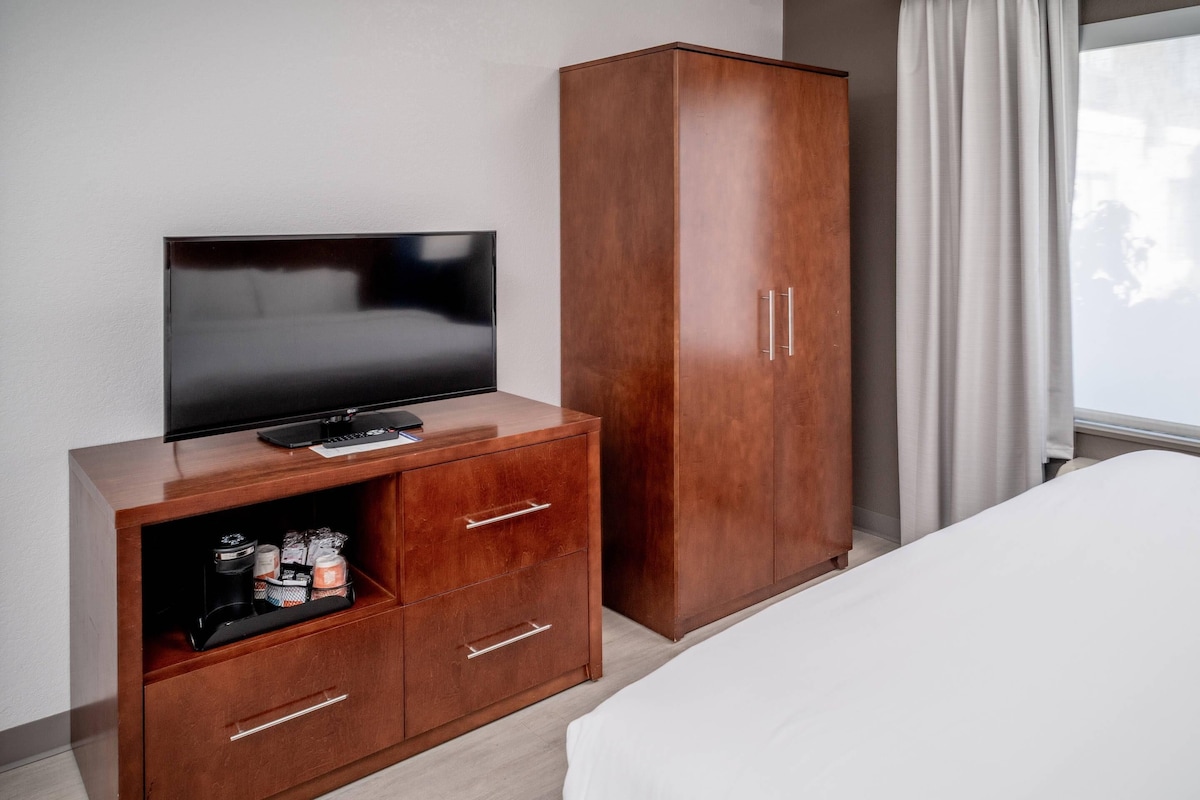Une chambre d’hôtel avec un téléviseur posé sur un meuble en bois, une armoire et un lit.
