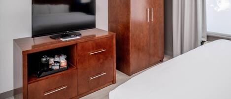 A hotel room with a TV on a wooden cabinet, a wardrobe, and a bed.