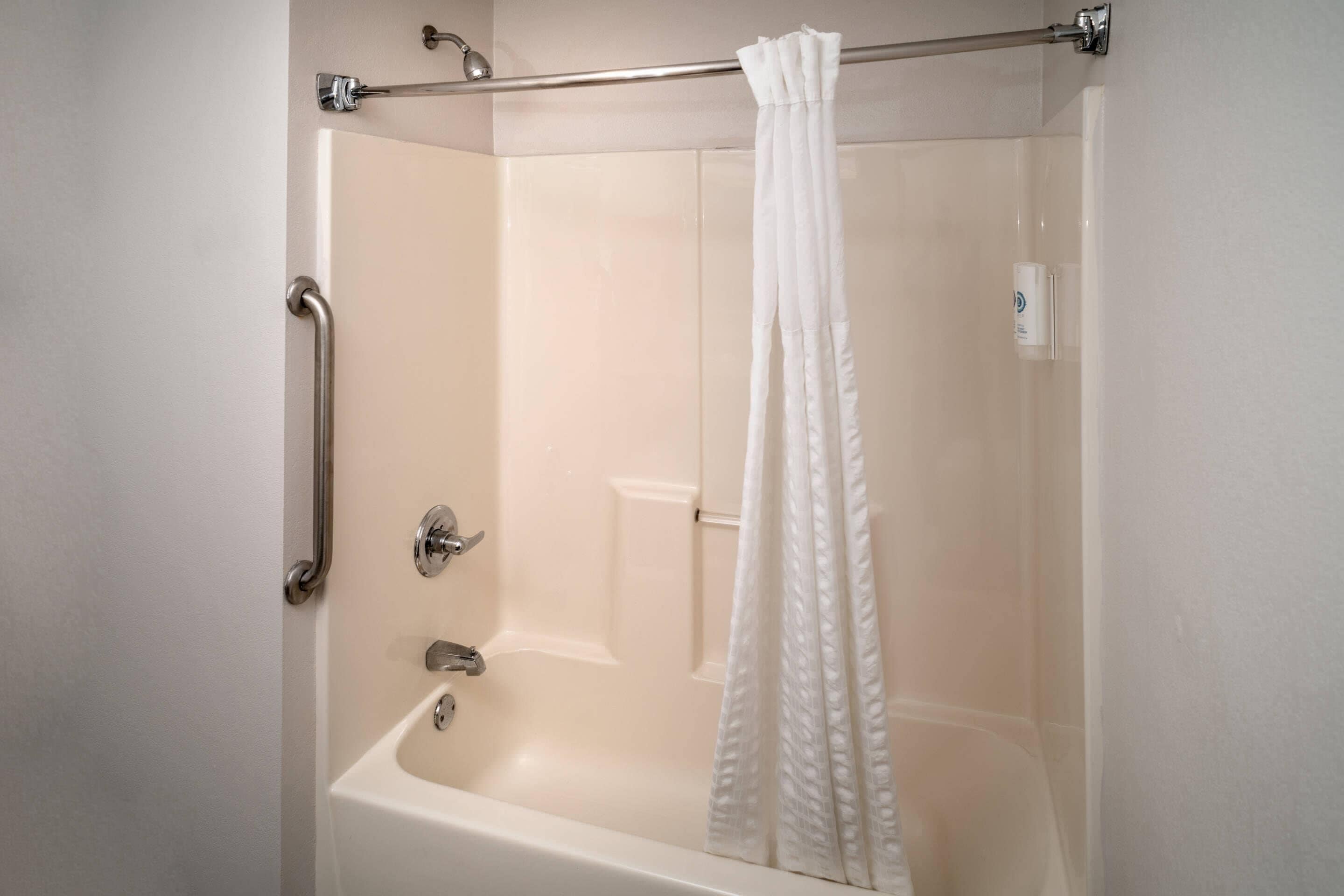 A walk-in shower with a white curtain, a grab bar, and a handheld showerhead.