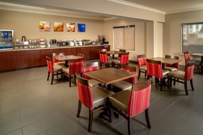 Een restaurantgedeelte van een hotel met verschillende tafels en stoelen, een buffet en een groot raam.