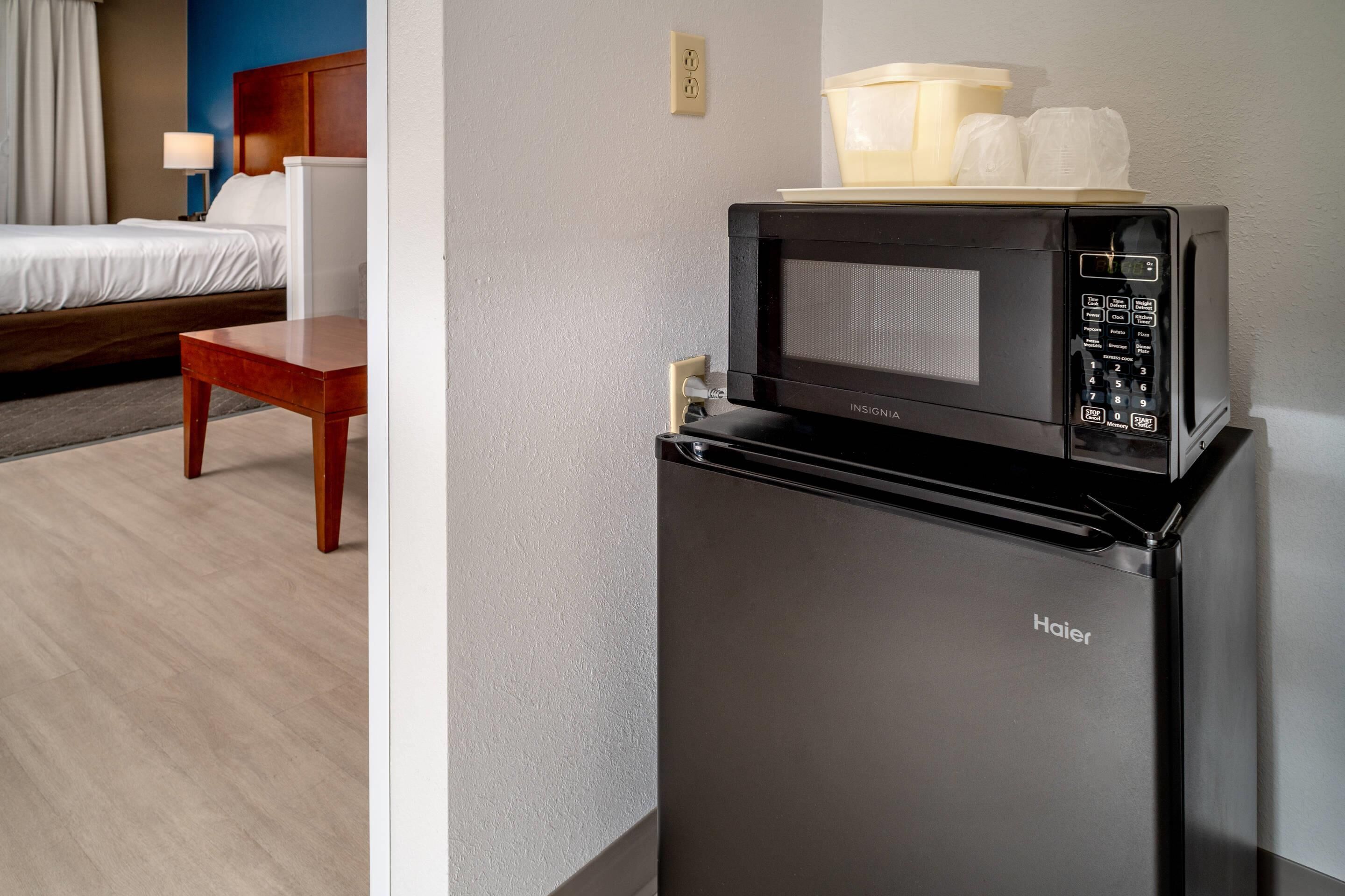 A compact kitchen area with a microwave and a refrigerator, a bed with a wooden headboard, and a bedside table.