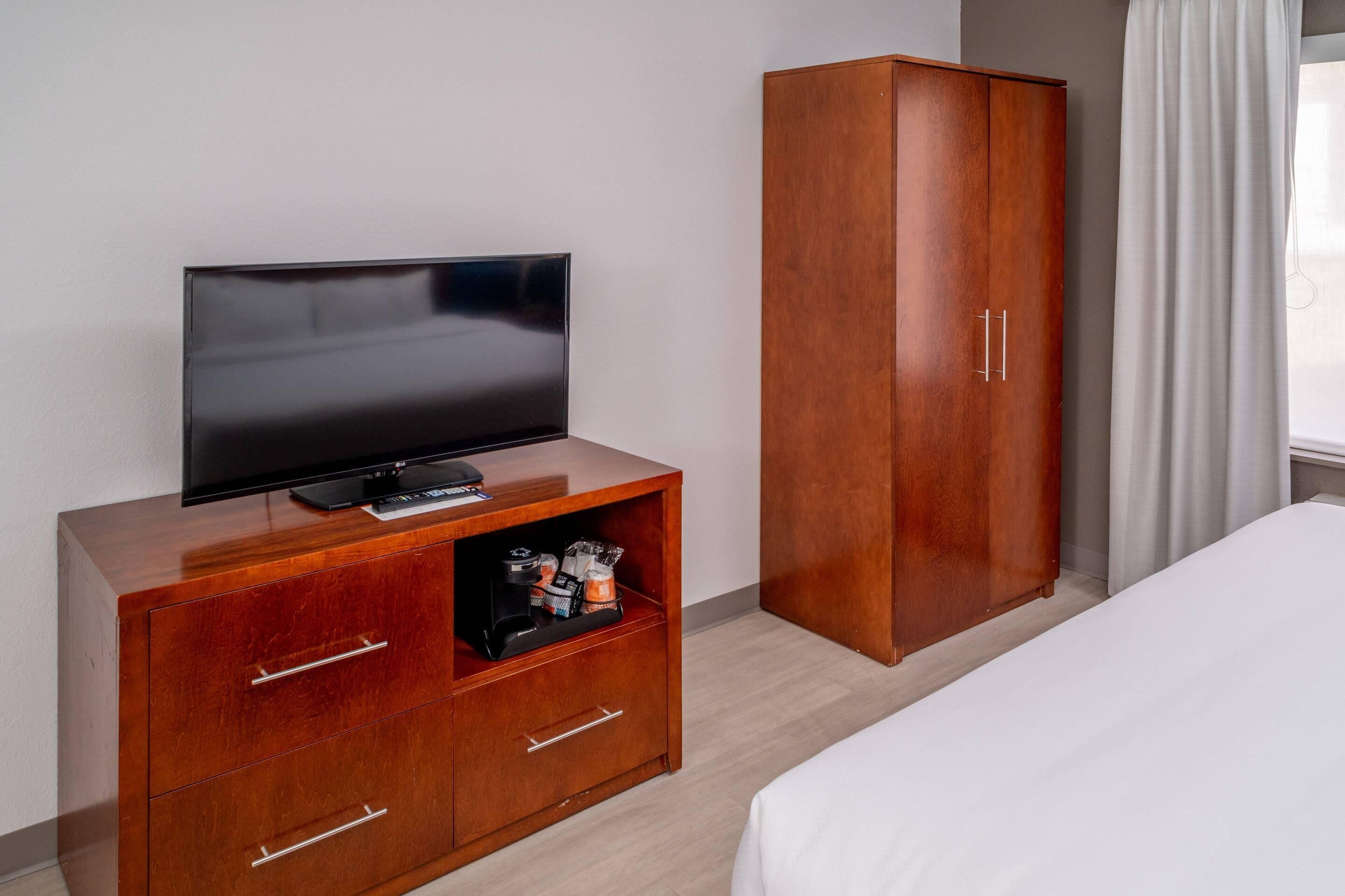 A hotel room with a wooden cabinet with a flat-screen TV, a wardrobe, and a bed.
