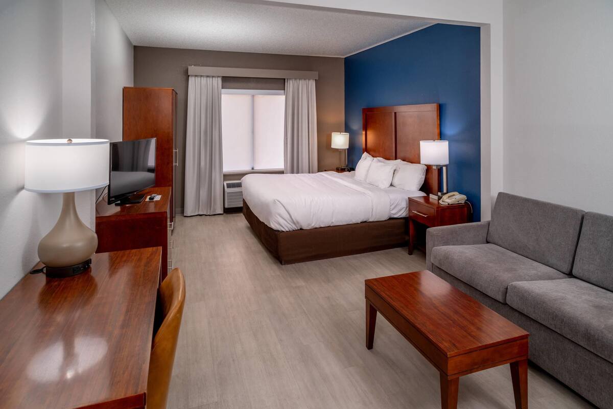 Een hotelkamer met een bed, een televisie, een bureau met lamp, een bank en een raam met gordijnen.