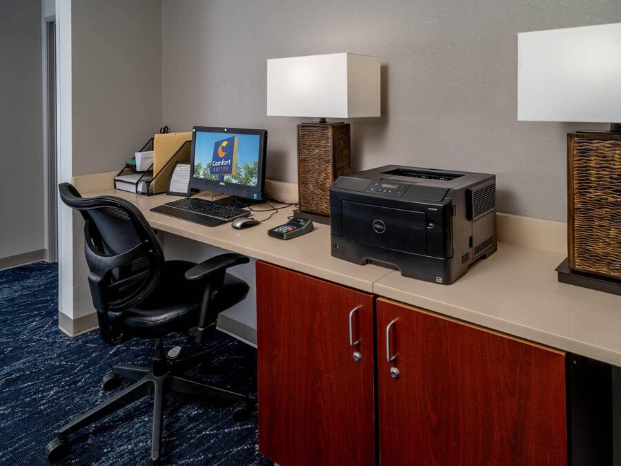 A hotel room with a desk, computer, printer, and two lamps.