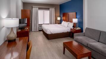 A hotel room with a bed, a desk, a television, a sofa, and a window with curtains.