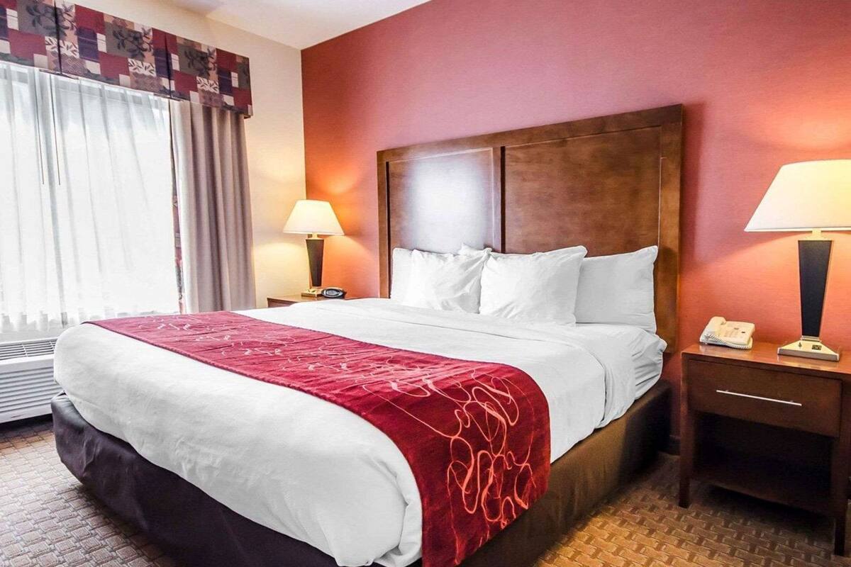 Een hotelkamer met een groot bed, twee nachtkastjes, een raam met gordijnen en een rode muur.