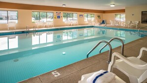 Une piscine intérieure à l’eau claire, avec des chaises longues blanches et une serviette posée sur une chaise.