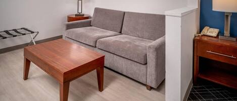 A room with a grey sofa, a wooden table, a lamp, and a telephone on a wooden side table.
