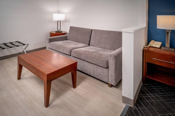 A room with a grey sofa, a wooden table, a lamp, and a telephone on a wooden side table.