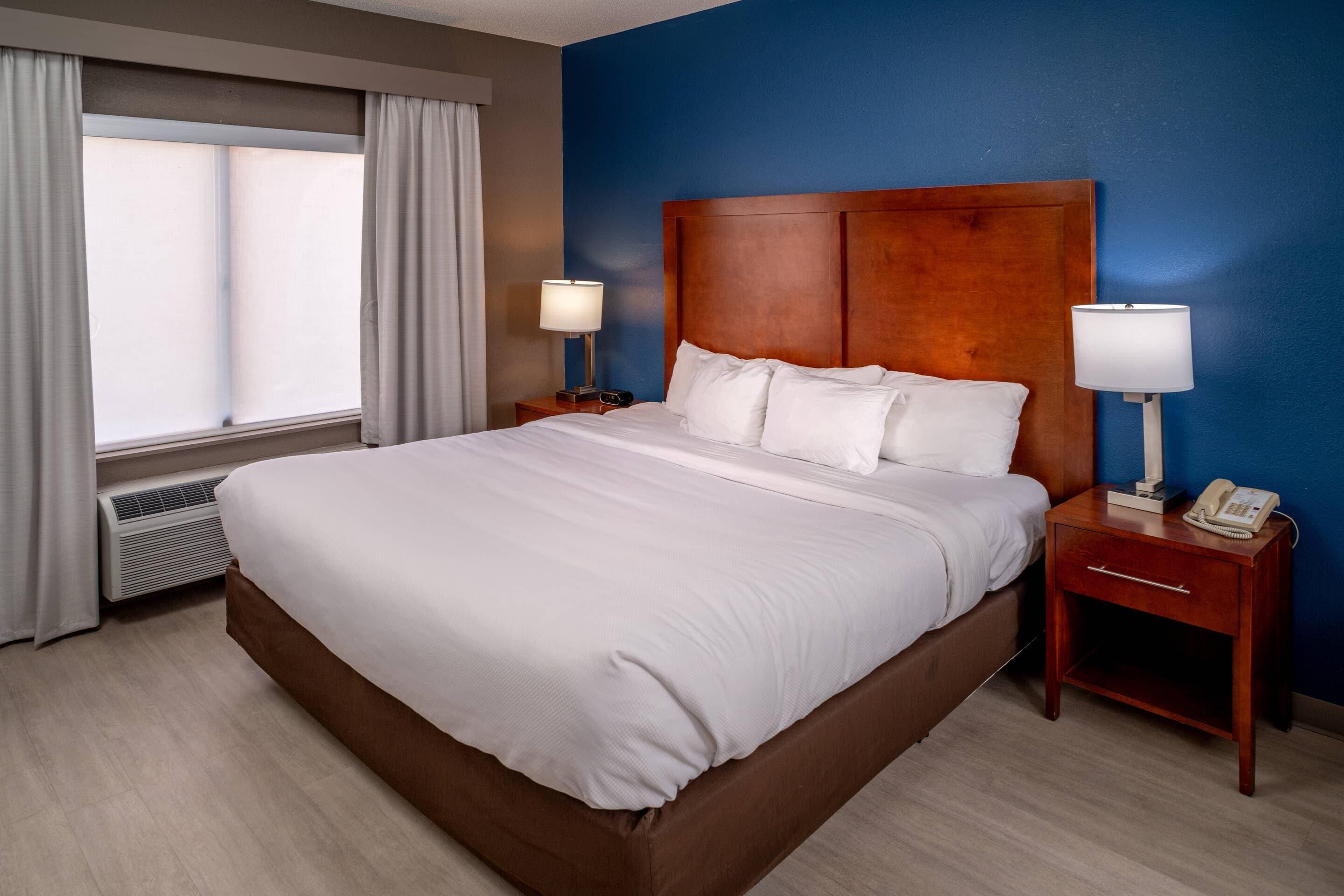 A hotel room with a large bed, two bedside tables with lamps, a telephone, and a window with curtains.