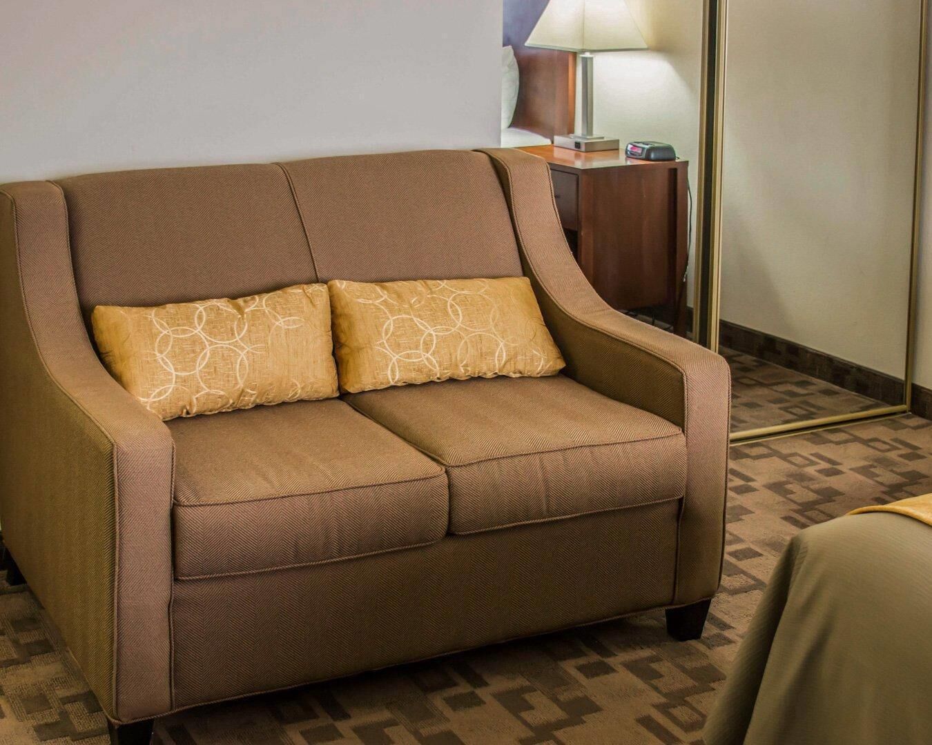 A brown sofa with two patterned cushions in a hotel room.