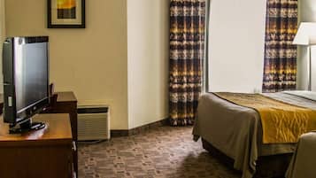 A hotel room with a bed, a TV, a desk, and a window with curtains.