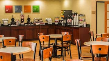 Un café avec des tables et des chaises en bois, un comptoir où l’on prépare différentes sortes de café, et des décorations murales.
