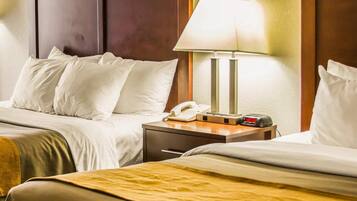 A hotel room with two beds, a bedside table with a lamp, a phone, and a clock.