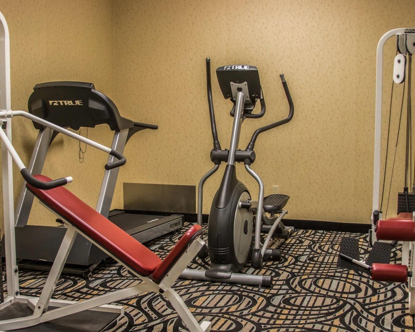 A hotel fitness room with a treadmill, elliptical, and weight bench.