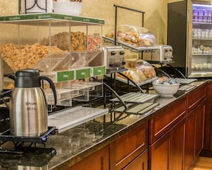 A breakfast bar with cereal, pastries, and a coffee machine.