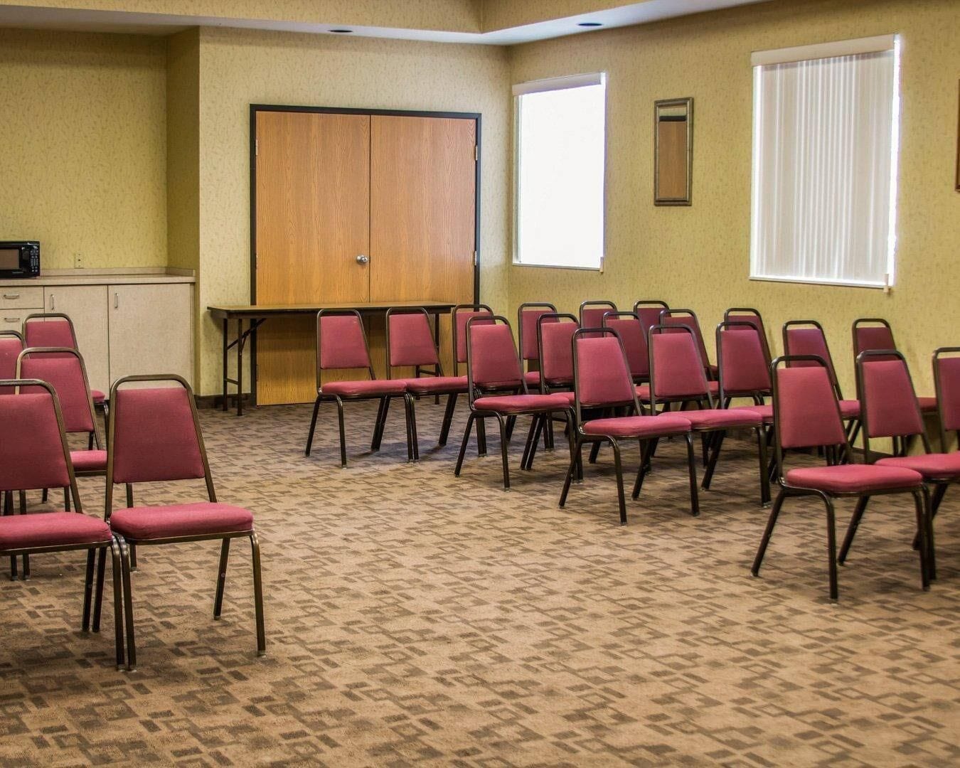 A conference room with rows of red chairs, a wooden door, and a projector screen.