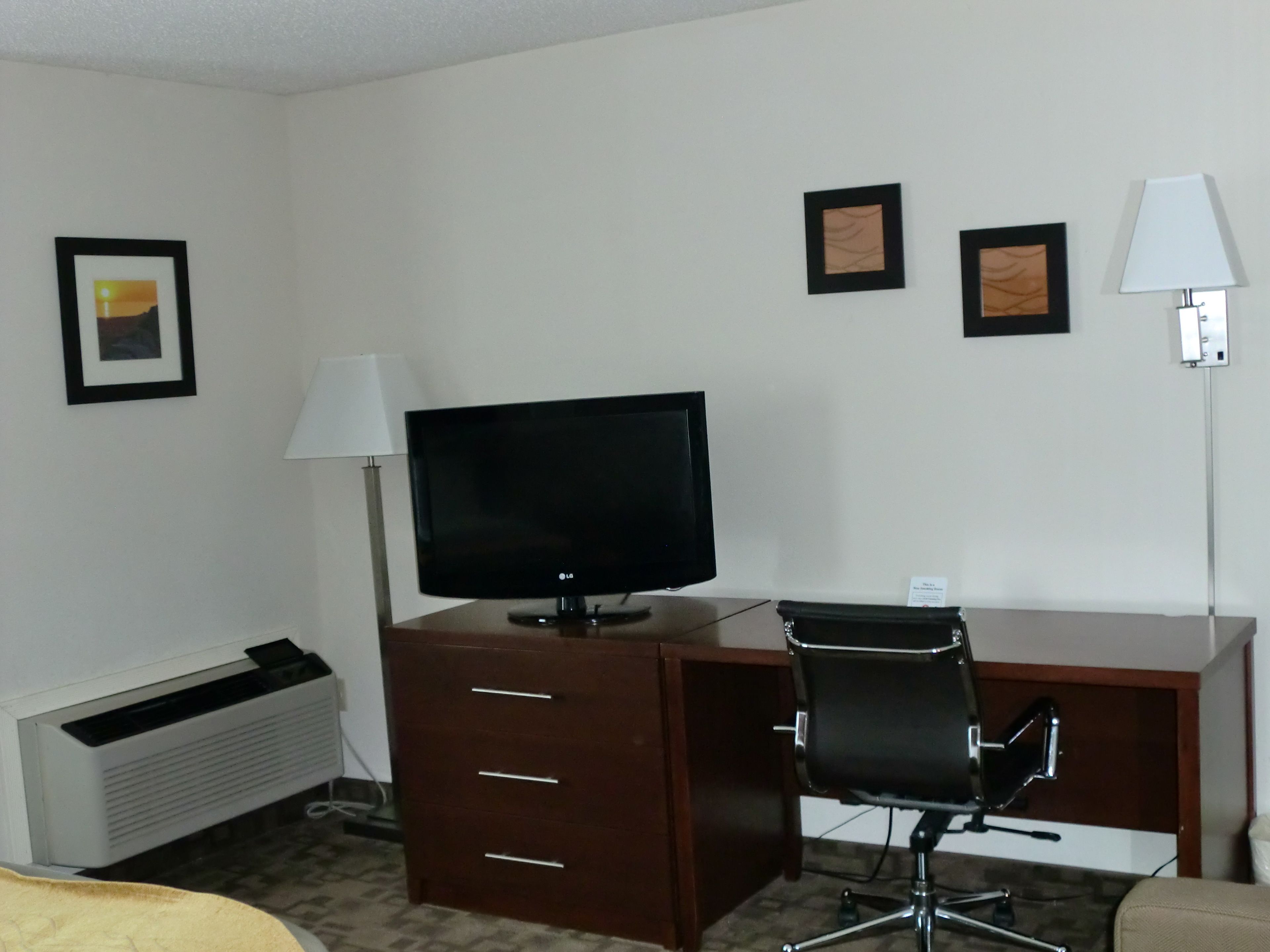 A hotel room with a desk, a television, a chair, and a lamp.