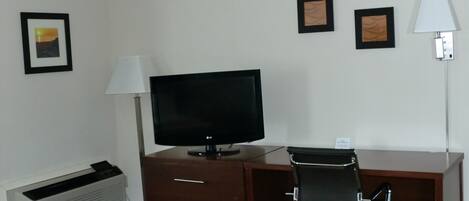 A hotel room with a desk, a television, a chair, and a lamp.