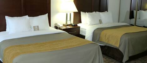 A hotel room with two beds, a nightstand with a lamp, a phone, and a mirror.