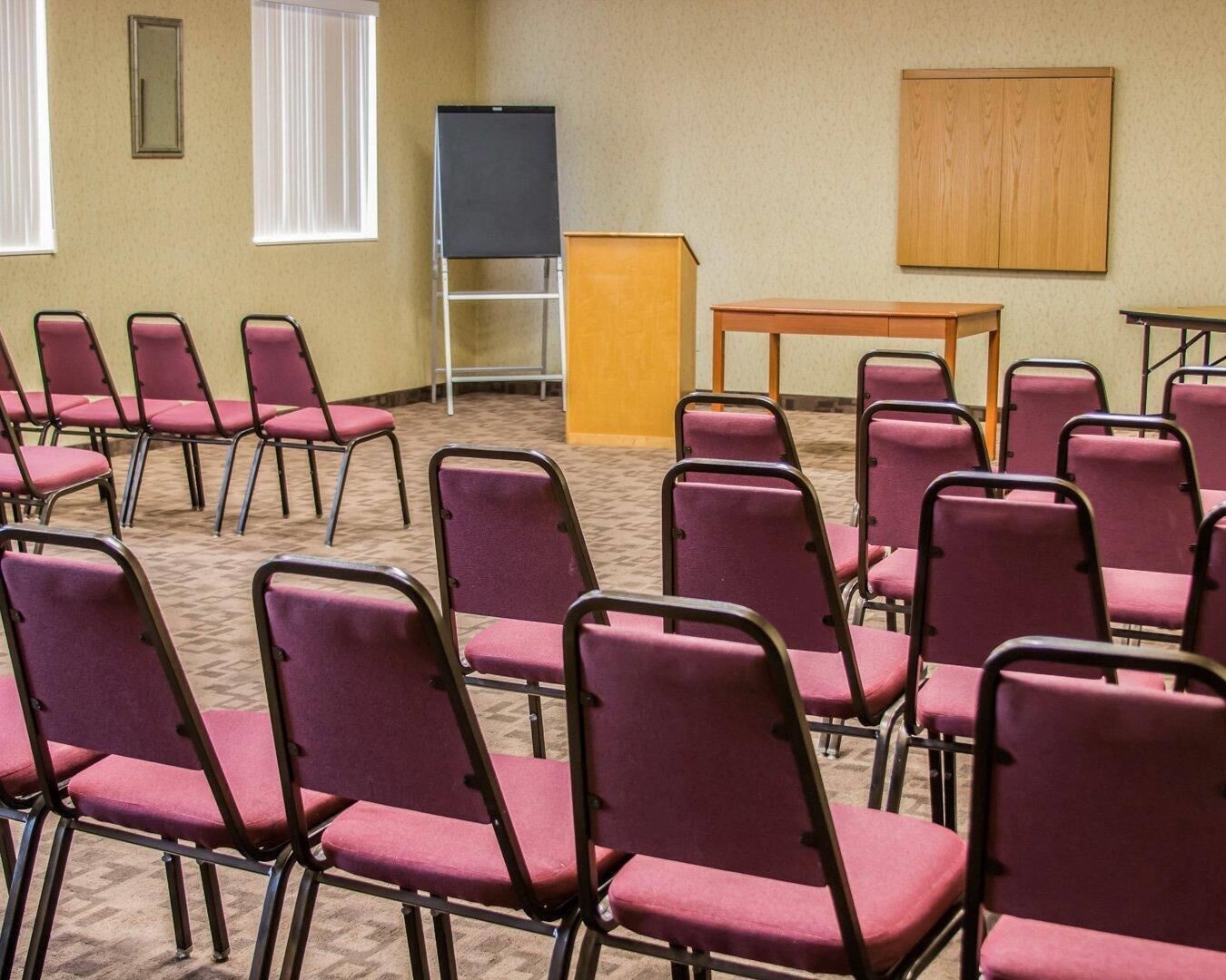 Un salón de conferencias con hileras de sillas moradas, un atril y una pantalla de proyector.