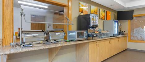 A buffet setup with a self-service station, a microwave, a coffee machine, and a refrigerator.