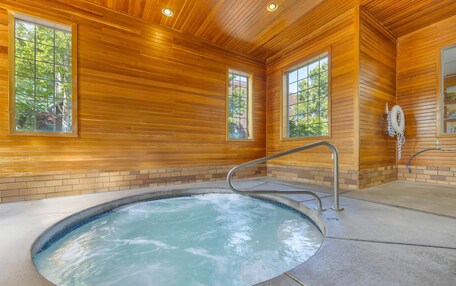 A wooden interior with a hot tub, large windows, and a brick wall.