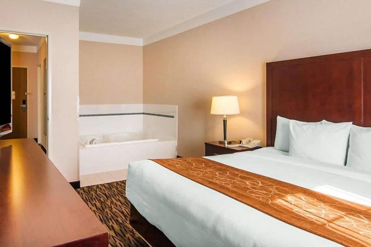 A hotel room with a bed, a desk, a lamp, a telephone, and a bathroom with a bathtub.