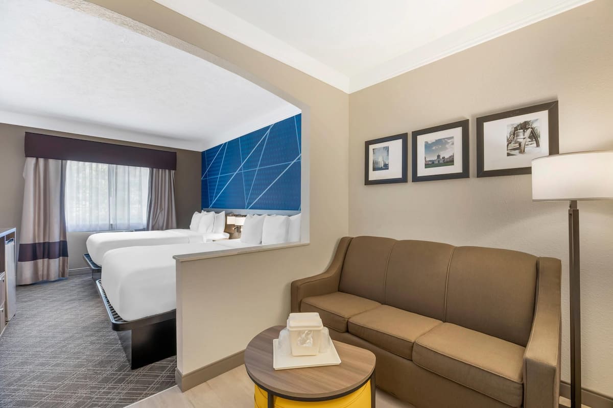 A hotel room with a bed, a sofa, a small table with a tray, and framed pictures on the wall.