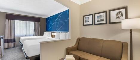 A hotel room with a bed, a sofa, a small table with a tray, and framed pictures on the wall.