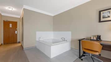 A modern bathroom with a large bathtub, a wooden door, and a desk with a chair.