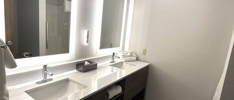 A modern bathroom with two sinks, a large mirror, and a towel rack.