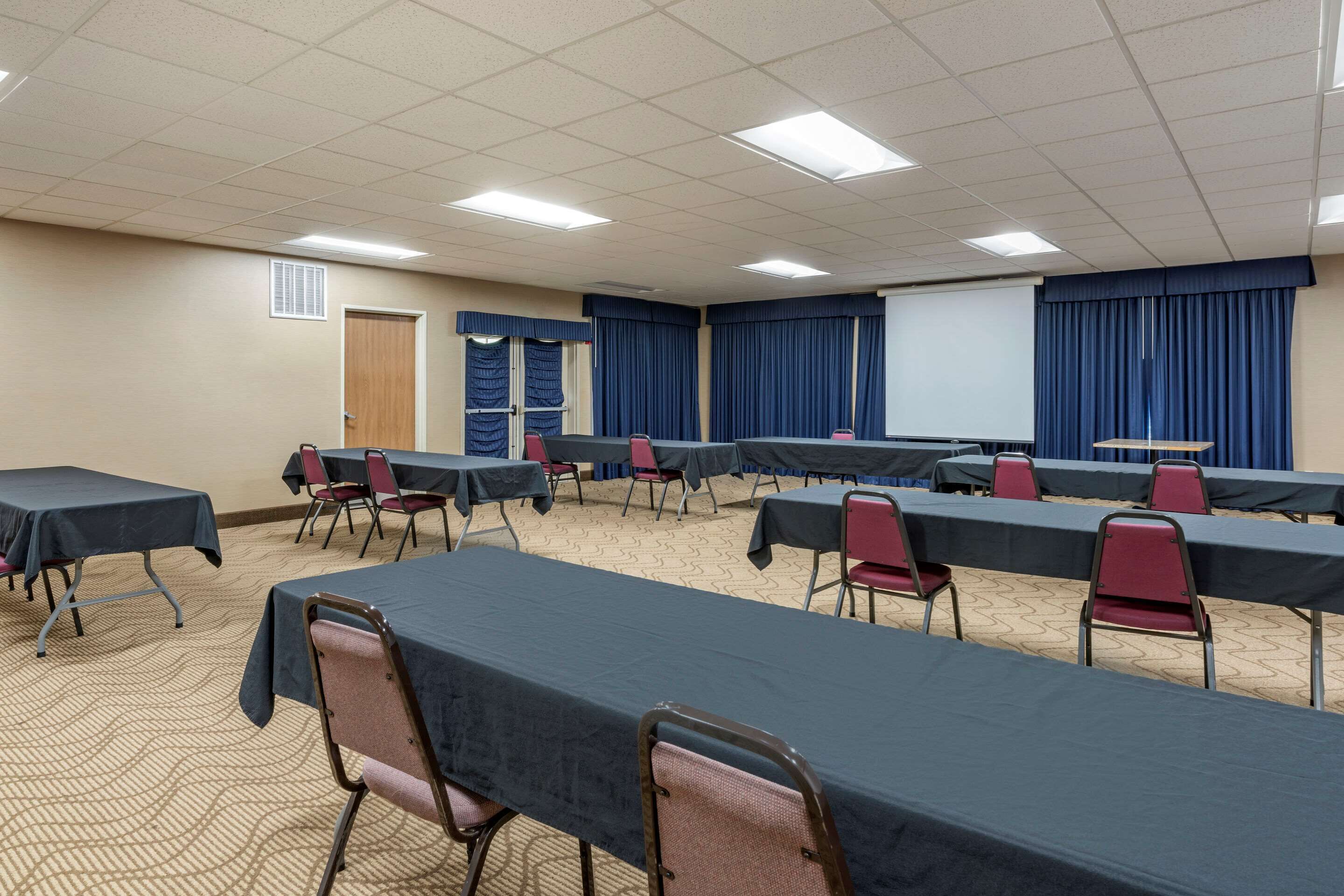 A conference room with long tables and chairs, a projector screen, and a door.
