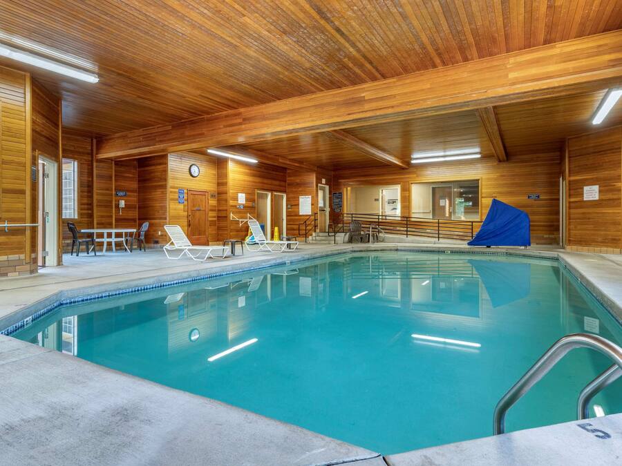 An indoor swimming pool with wooden walls, a clock, and lounge chairs.