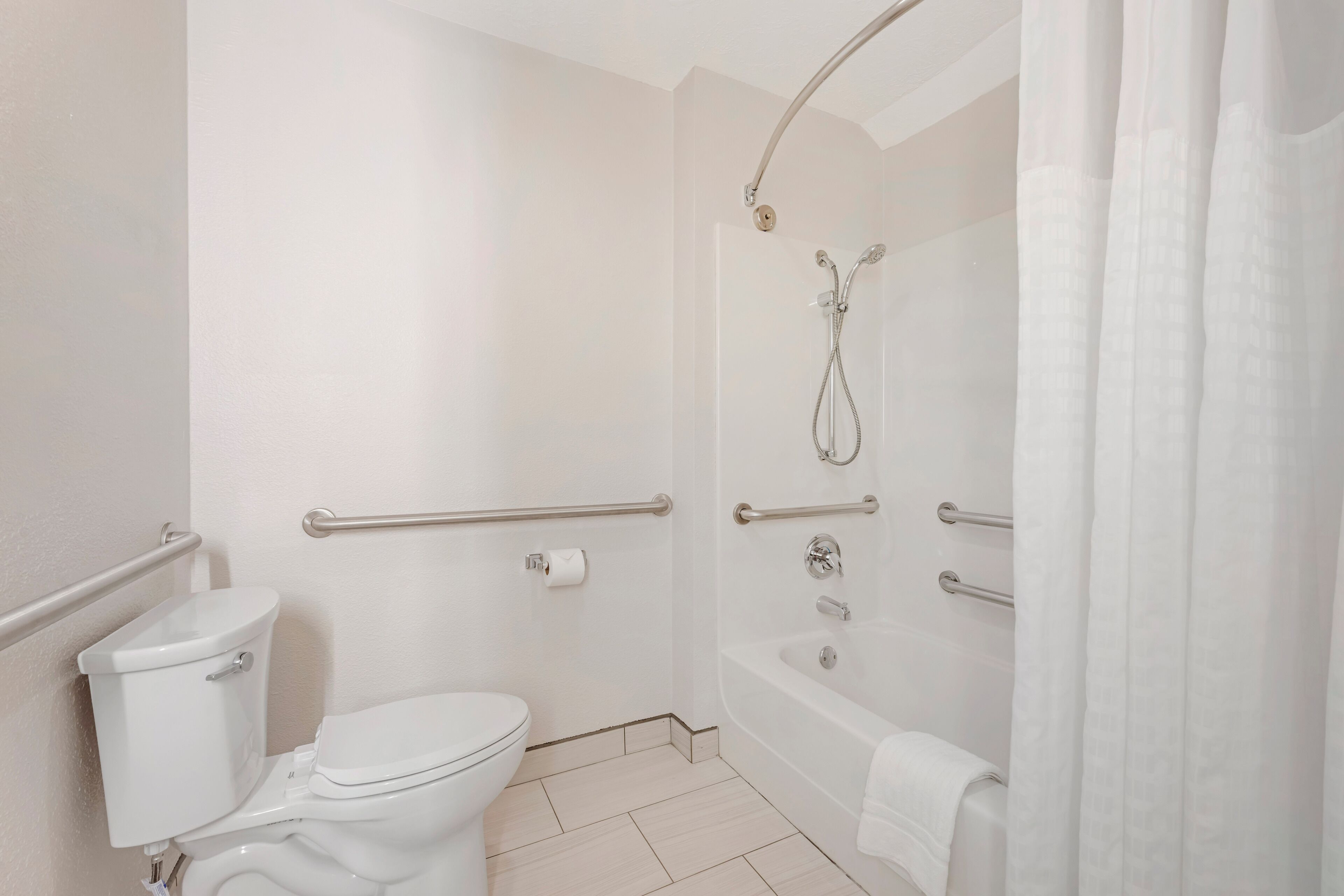 A bathroom with a toilet, a shower, and a bathtub, equipped with grab bars and a towel rack.